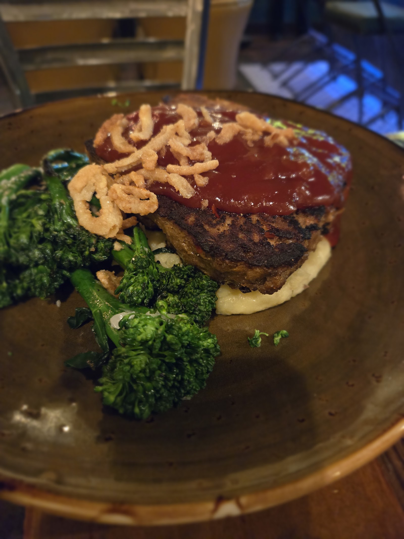 Thick patty with red glaze and crispy onion strings on mashed potatoes, served with sautéed greens, in Glacier National Park.