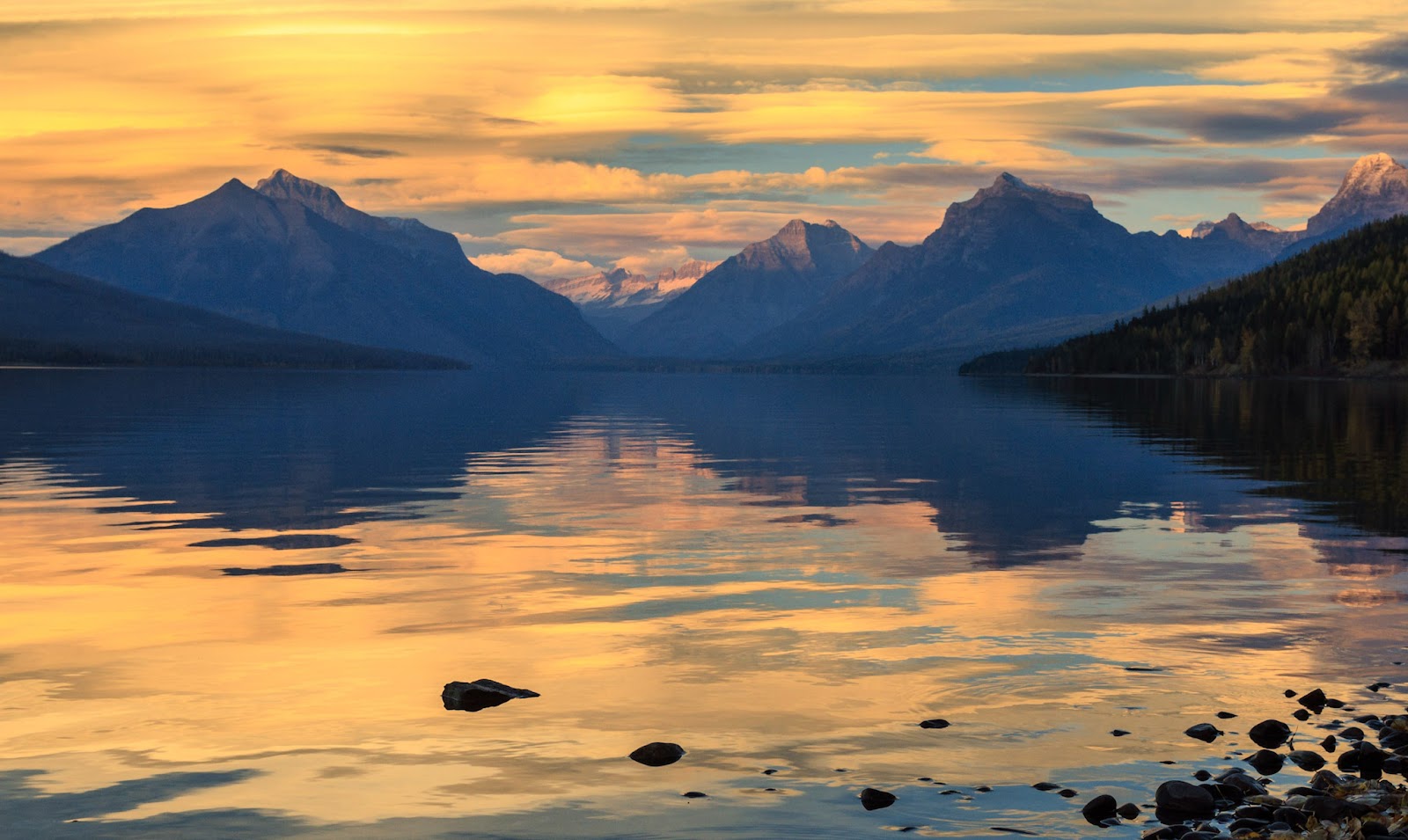 Apgar Campground shoreline along Lake McDonald with snowy Glacier peaks at sunset in Glacier National Park.