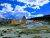 Blue sky with clouds over Liberty Cap travertine cone in Yellowstone National Park, featuring a wooden boardwalk, yellowish terraces, and hikers.