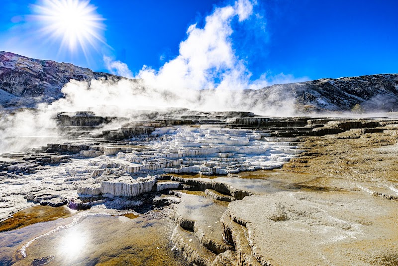 Steaming white travertine terraces at Liberty Cap, Yellowstone National Park, under a bright blue sky.