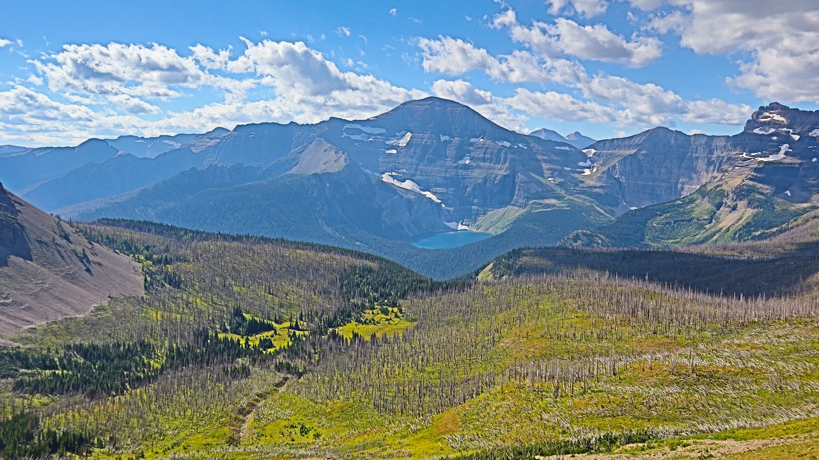 Chapman Peak overlooks a glacial valley with a turquoise lake and snow-dusted peaks in Glacier National Park.