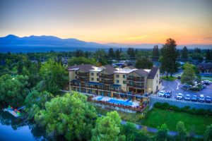 Exterior view of a multi-story hotel along the Whitefish River with mountain backdrop near Glacier National Park.