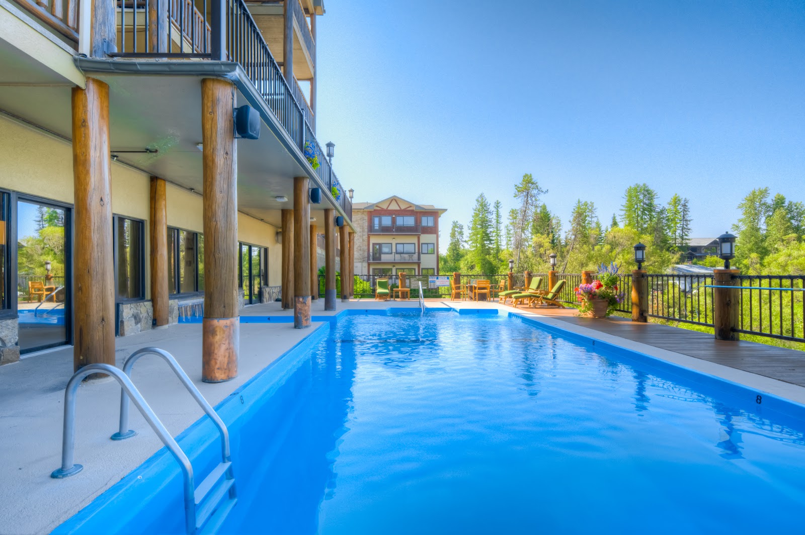 Outdoor pool at a lodge along the Whitefish River in Glacier National Park, with bright blue water and wooden columns supporting the balcony above.