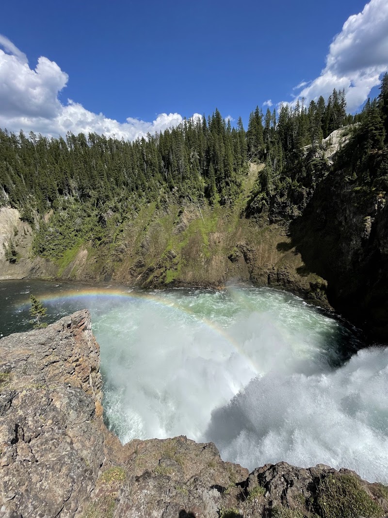 Upper Falls View in Yellowstone National Park shows a plunging turquoise river between rocky cliffs with a rainbow above.