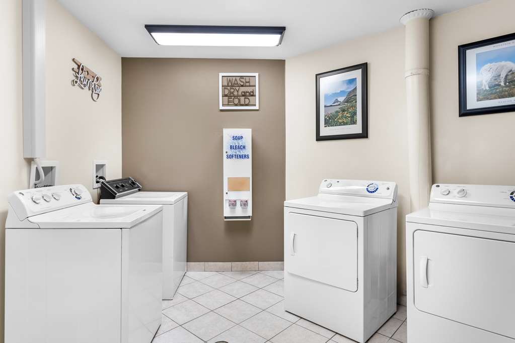Laundromat with four white top-loading machines, beige walls, framed landscape photos, and a soap dispenser in Glacier National Park.