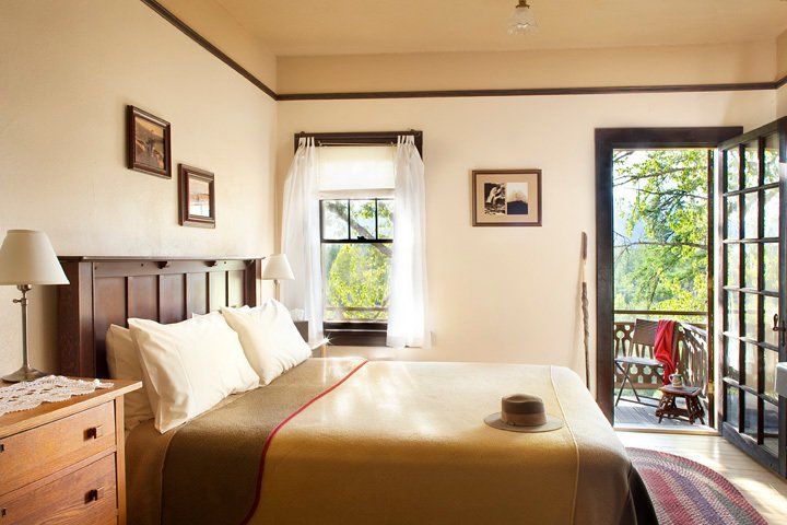 Cozy guest room at Glacier National Park featuring a dark wood headboard, white curtains, and a door opening to a balcony.