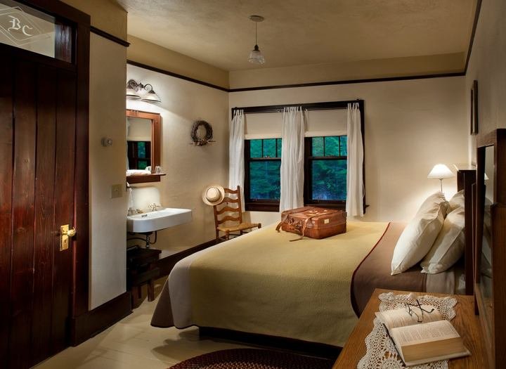 Chalet-style hotel room with a large bed, window views, and luggage on a dresser in Glacier National Park.