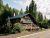Chalet-style lodge along a forested Glacier National Park road, with a wooden deck, flags, and dense pines nearby.
