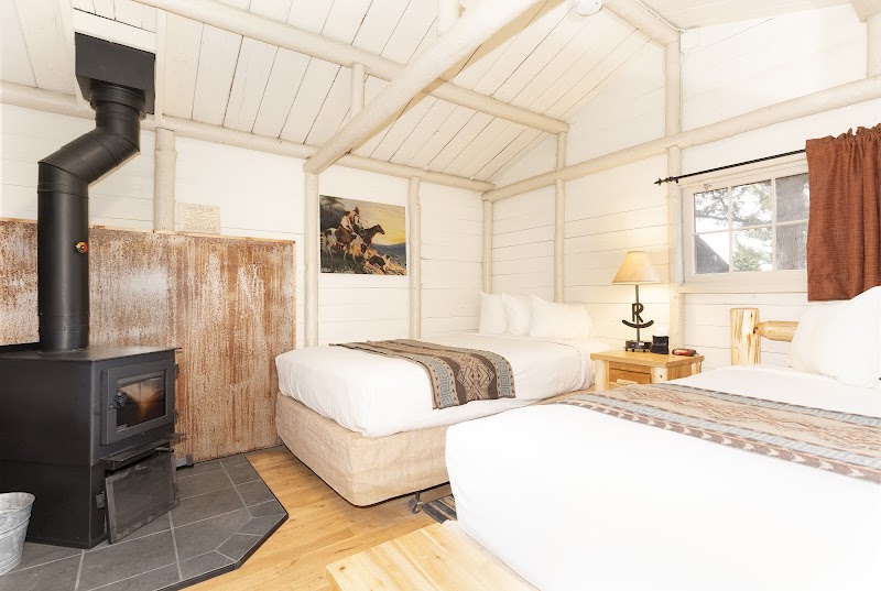 Cozy Yellowstone National Park cabin interior with two queen beds, a wood stove, rustic beams, and a bedside lamp.