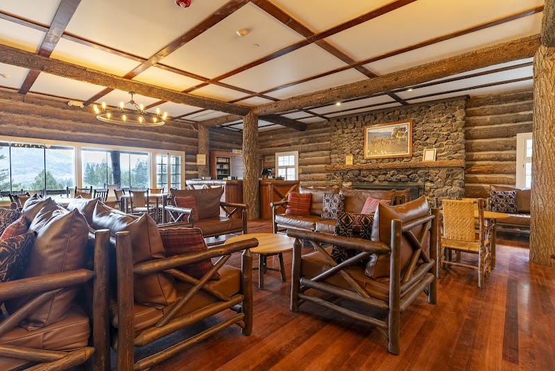 Cozy lodge living area with log furniture, a stone fireplace, wooden beams, and warm floors at Yellowstone National Park.