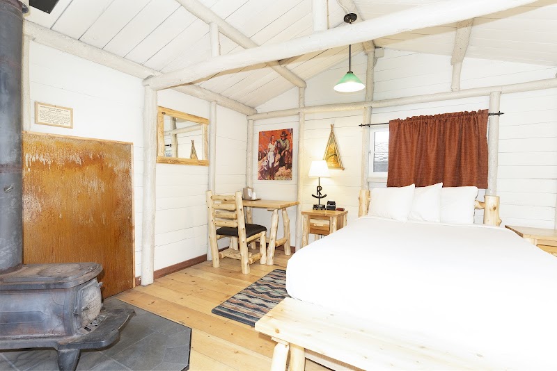Cozy Yellowstone National Park cabin bedroom with a white duvet bed, wood stove, rustic desk, chairs, and a striped rug.
