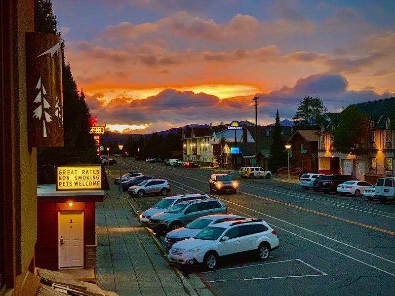 Sunset over a Yellowstone National Park town center with parked cars, motel signage, and lit shops along the street.