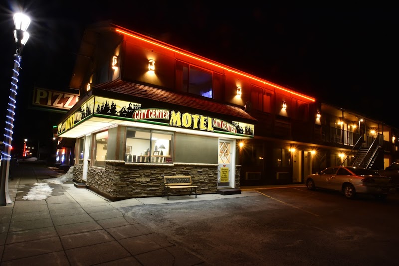 Yellowstone National Park motel at night with a stone facade, neon roofline, glowing sign, exterior corridor, and a parked car.