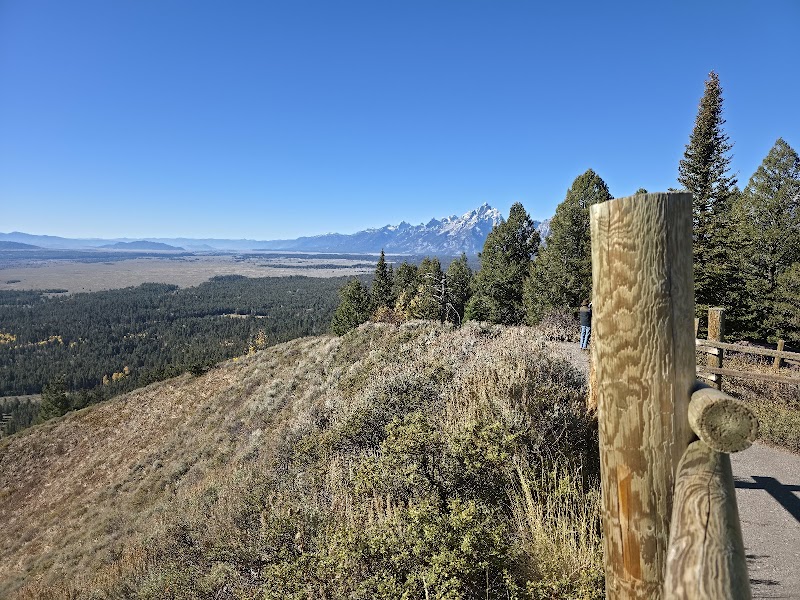 Trail overlook on Signal Mountain Summit with a wooden fence, pines, and distant Yellowstone National Park peaks.