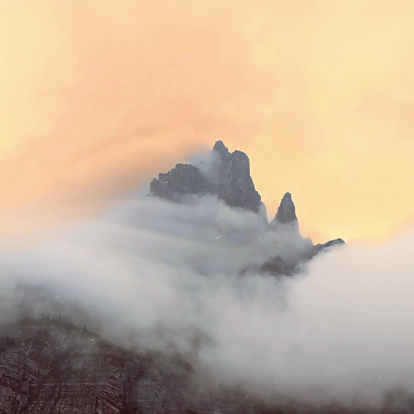Jagged Pyramid Peak rises above a thick sea of clouds with a warm orange sky, Glacier National Park.