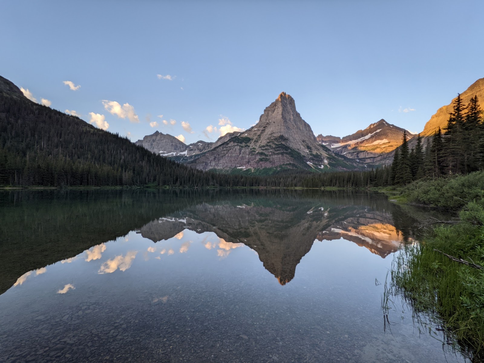 Pyramid Peak rises above a calm alpine lake in Glacier National Park, with evergreen forests and a perfect mountain reflection.