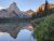 Pyramid Peak rises above a glassy alpine lake with evergreen shoreline in Glacier National Park, at dusk.