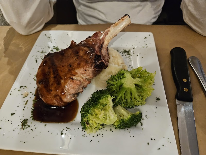 Juicy bone-in lamb chop with glossy sauce beside mashed potatoes and broccoli florets on a square plate in Yellowstone National Park.