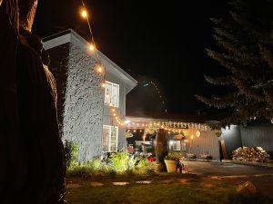 Boutique inn exterior in Glacier National Park lit by warm string lights at night, with a stone wall and cozy garden.