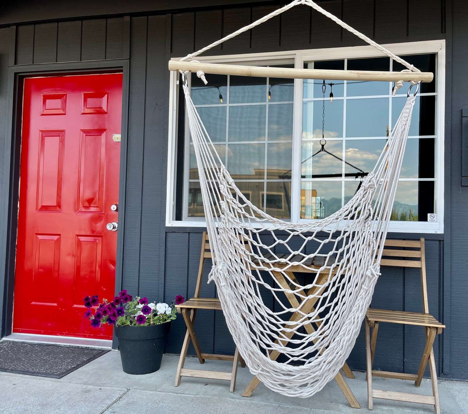 Exterior view of a lodge porch in Glacier National Park with a white rope hammock hanging between a large window and a bright red door.