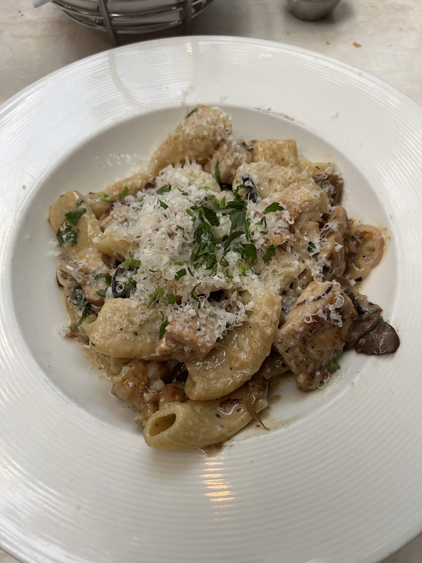Creamy pasta with rigatoni, mushrooms, and herbs topped with grated cheese in a white bowl, Glacier National Park.