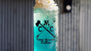 Bright teal iced beverage served in a mason jar at a Glacier National Park cafe, topped with whipped cream.