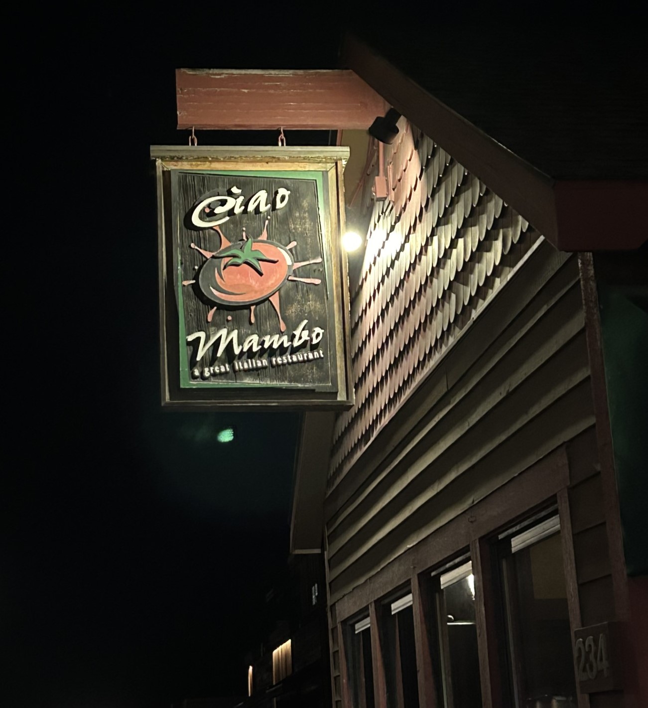 Exterior view of a wooden building at night featuring a rustic sign for a mountain Italian restaurant in Glacier National Park.