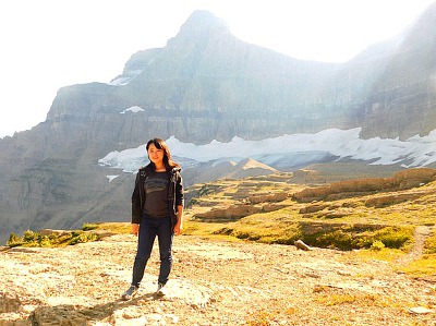 Matahpi Peak overlook in Glacier National Park with rugged alpine terrain and distant snow patches under bright sky.