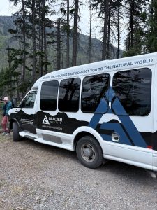 Glacier National Park scene with a forested roadside educational van parked among tall pines.