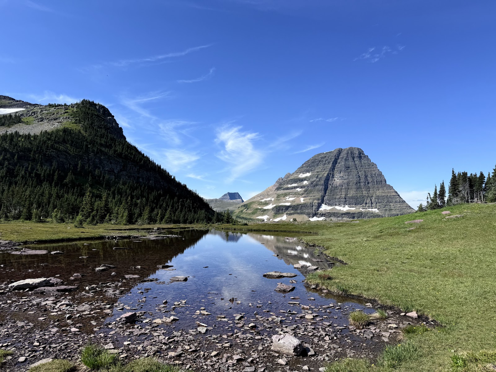 Swiftcurrent Lake in Glacier National Park reflects a pyramidal peak, evergreen forests, and a bright blue sky.