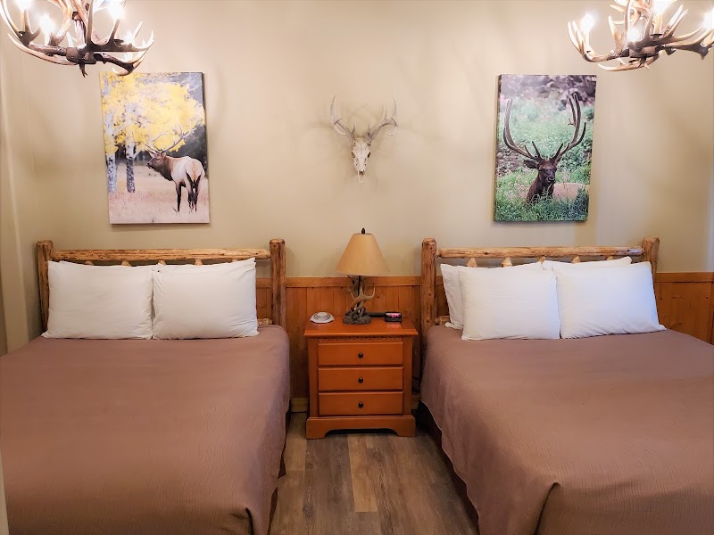 Two-queen lodge room in Glacier National Park featuring rustic log headboards and antler wall decor.