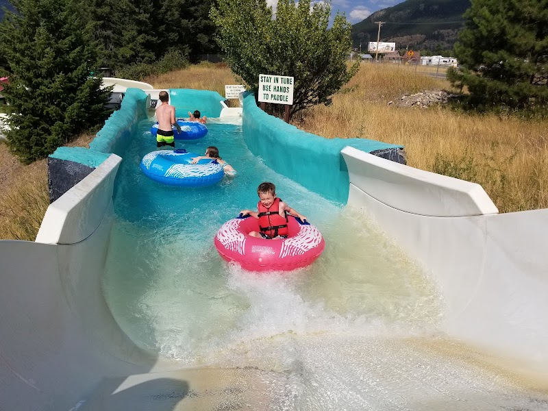 Families ride a winding water-slide pool at a lodge near Glacier National Park under bright summer skies.