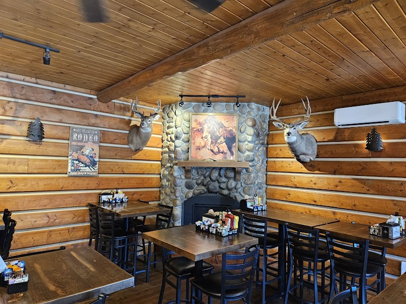 Rustic Yellowstone National Park dining room with log walls, two mounted deer heads, a stone fireplace, and wooden tables.