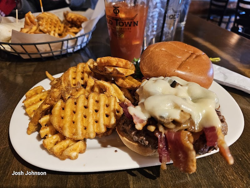 Cheeseburger with bacon and melted cheese, waffle fries and onion rings on a white plate with a drink in Yellowstone National Park.