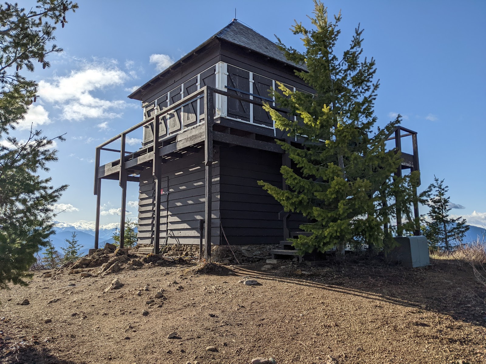 Apgar Lookout Trailhead viewpoint in Glacier National Park features a rustic wooden lookout building atop a rocky hill with surrounding pines.