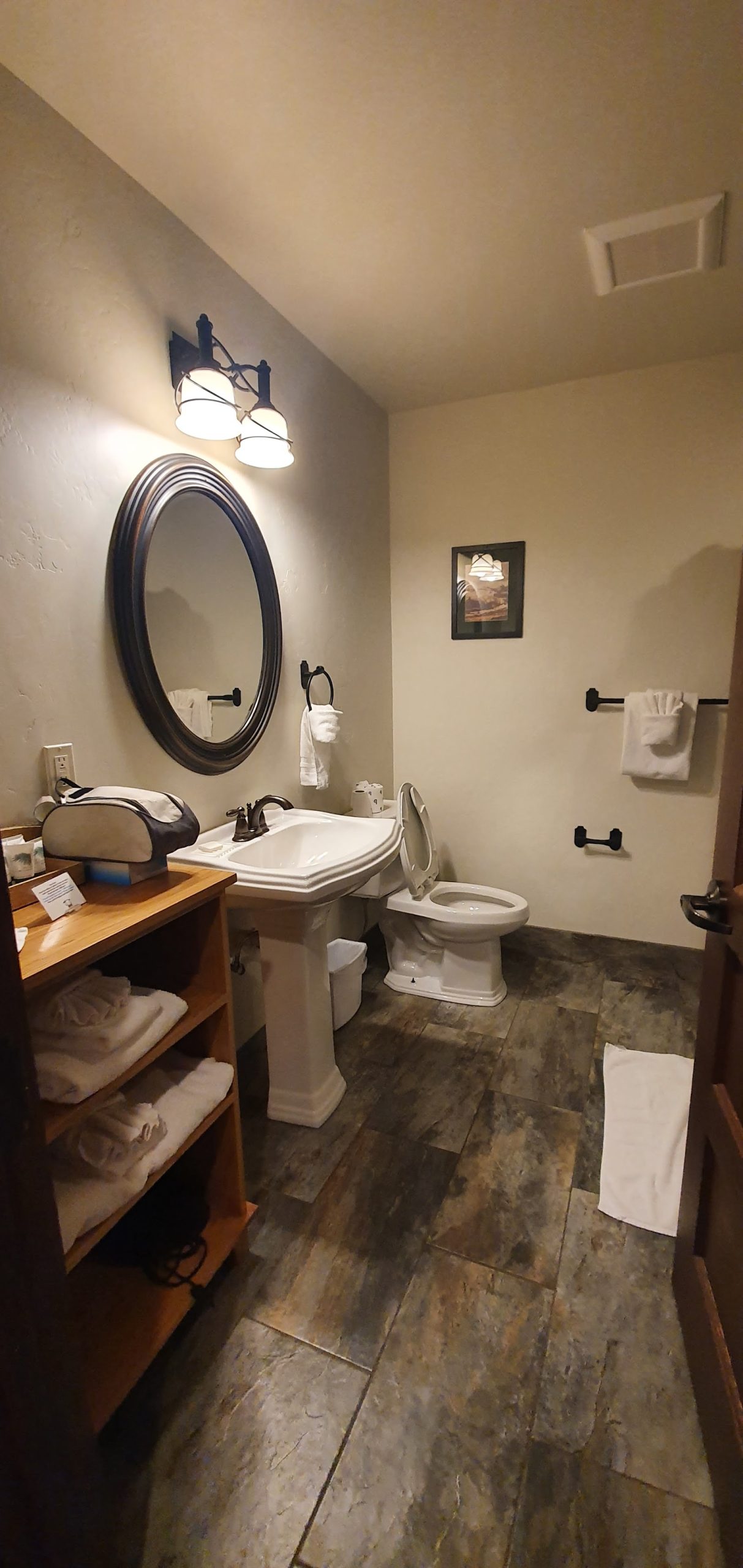 Glacier National Park lodge bathroom with pedestal sink, large oval mirror, and warm lighting.