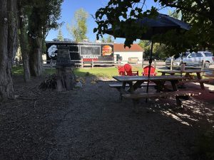 Outdoor seating area with wooden picnic tables and a black food truck in Whitefish near Glacier National Park.