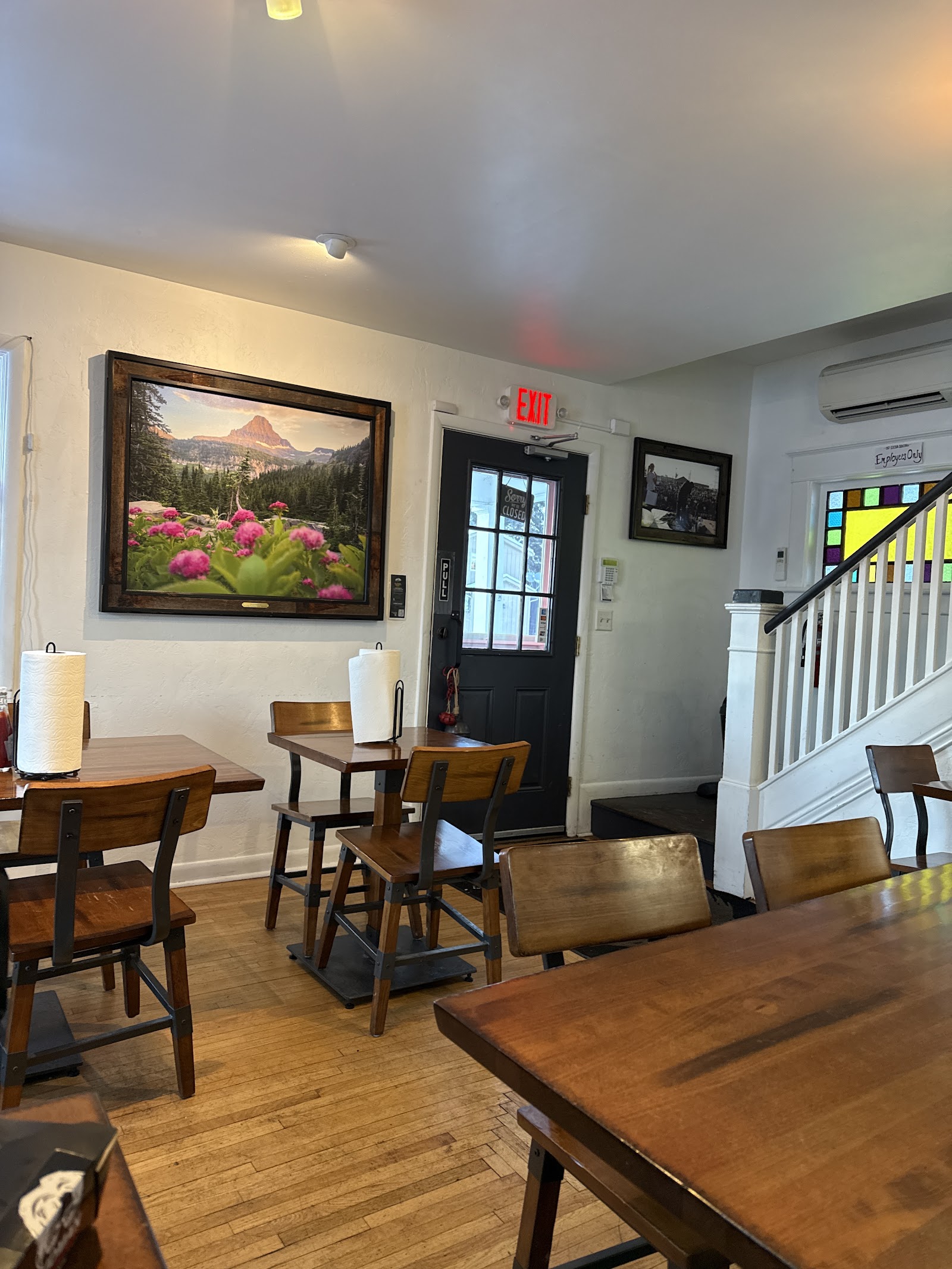 Interior of a casual restaurant in Glacier National Park near Whitefish, with wooden tables and a large framed mountain photograph on the wall.