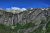 Gunsight Mountain rises above a rugged Glacier National Park valley with waterfalls and patches of lingering snow under a clear blue sky.