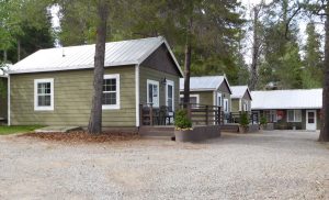 Lodging row at Glacier National Park with olive siding cabins, white-framed windows, and metal roofs along a gravel road.