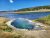 Mud Volcano pool at Yellowstone National Park showing a steaming blue-green pool surrounded by mineral terraces and grasses under a clear sky.