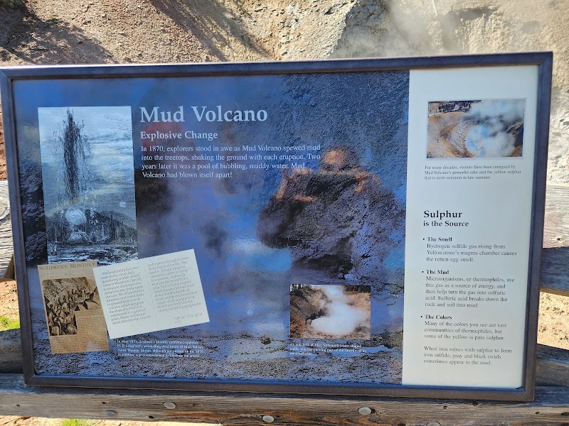 Informational sign about Mud Volcano with photos and text panels set on a wooden railing at Yellowstone National Park.