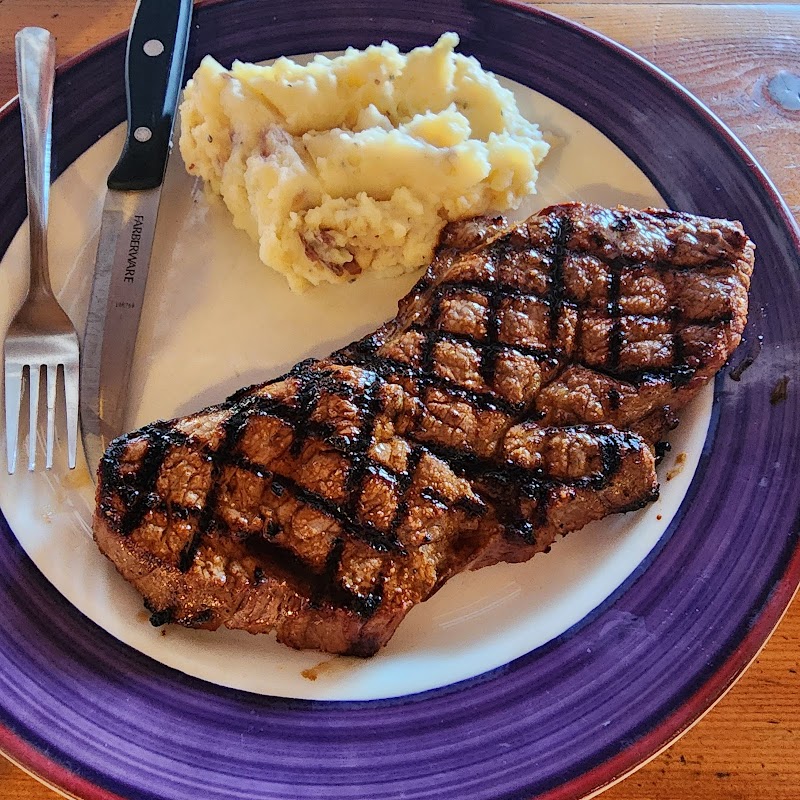 Juicy grilled steak with crosshatch marks and mashed potatoes on a white plate with a purple rim, Yellowstone National Park.