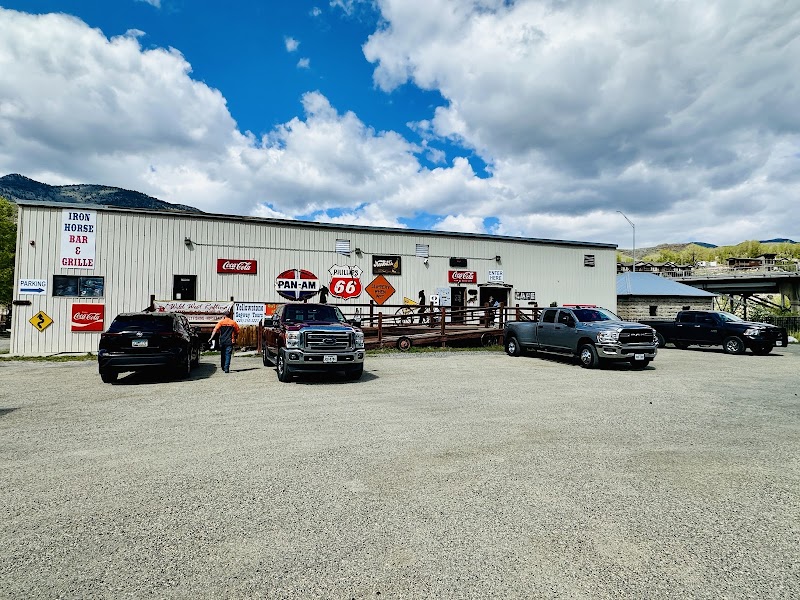 Yellowstone National Park scene with a long light-gray metal building, parked trucks, and Route 66 and Coca-Cola signs along the facade.