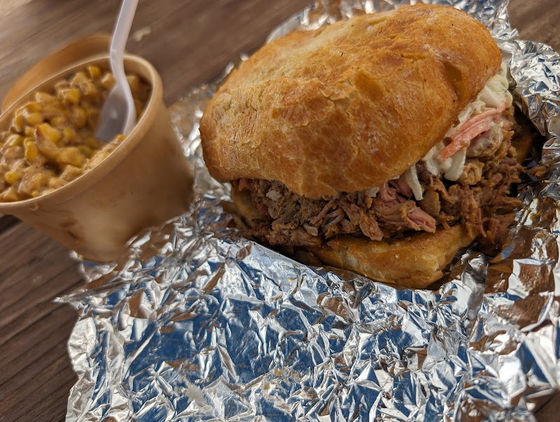 Pulled meat sandwich on a golden bun wrapped in foil, with a cup of bean and corn relish beside it at Yellowstone National Park.