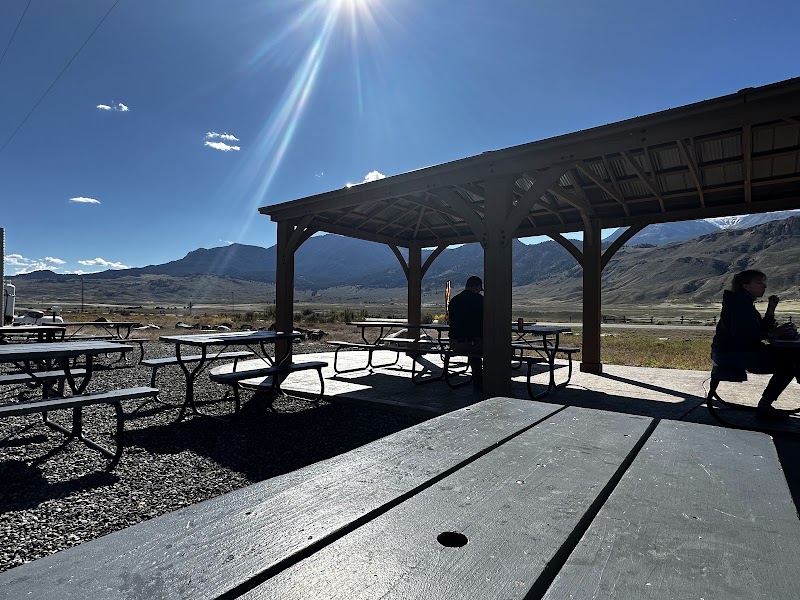 Sunlit outdoor pavilion with wooden beams and picnic tables against a mountain backdrop at Yellowstone National Park.