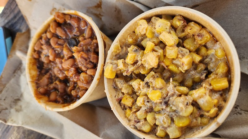 Two takeout bowls on parchment show baked beans and a cornmeal hash with corn and meat, at Yellowstone National Park.
