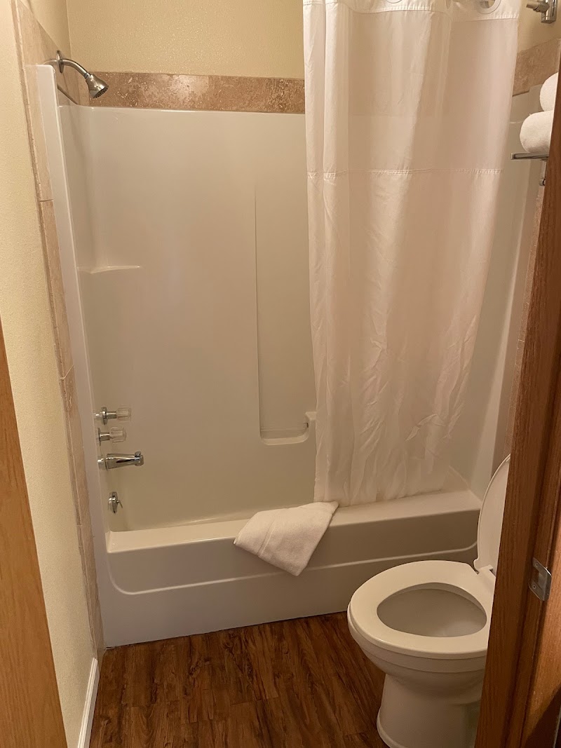 Cozy bathroom with a white bathtub and shower curtain, towel on the tub edge, toilet, and wood-look flooring in Yellowstone National Park.
