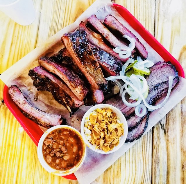 Sliced smoked ribs on a red tray with onions, plus beans and crunchy fried topping, in Yellowstone National Park.