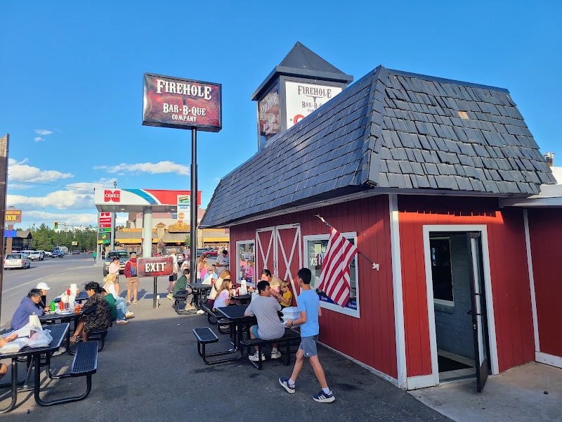 Red barn-style restaurant with outdoor picnic tables full of diners, flags, and a blue sky in Yellowstone National Park.